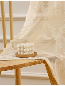 Detail of beige French vintage lace curtain with damascus pattern draped on wooden chair
