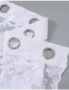 Detail of white French lace curtain with floral patterns and silver metal grommets