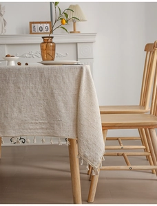 Close-up of beige linen tablecloth featuring delicate tassel edges in a warm home setting