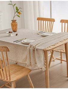 Detailed view of oatmeal linen tablecloth with handcrafted tassel edges on wooden table