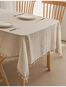 Close-up of beige linen tablecloth with elegant fringe tassels in a cozy dining room