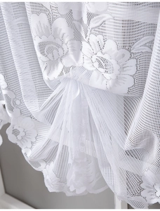 Close-up of white lace curtain with intricate floral patterns and wavy scalloped edges
