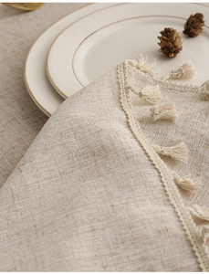 Detailed macro view of beige linen tablecloth with delicate lace and handmade tassels