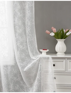 Detail of white semi-sheer lace curtain with elegant branch pattern in a cozy room