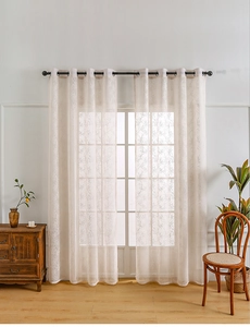 Close-up of off-white lace curtains with branch patterns and metal grommet details