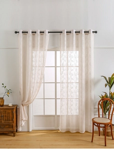 Detail of beige lace curtains with tree branch patterns and metal grommet top design