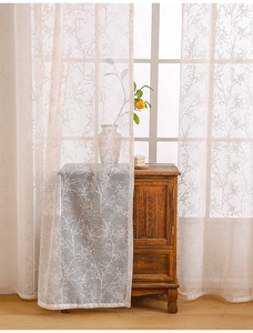 Detail of semi-sheer lace curtain with delicate branch pattern in a warm natural light setting