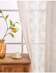 Close-up of beige lace window curtain with delicate branch pattern and mesh texture