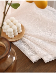Close-up of white lace curtain with delicate leaf patterns on a dark wooden table