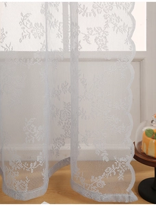 Detail of white rose lace curtain with scalloped edges and delicate floral mesh texture