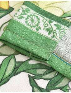 Close-up of linen fabric showing green leaf floral pattern and durable double-stitched hem