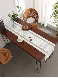 Detail of white woven table runner with diamond pattern lace edges and brown tassels