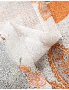 Close-up of thick textured linen fabric with orange floral prints and lace edge details