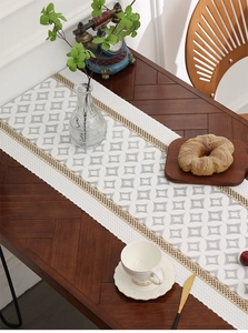 Close-up of white table runner with grey geometric diamonds and beige woven tassels