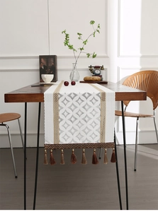 Detailed view of white hollow lace table runner with geometric patterns and brown tassels