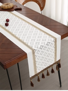 Detail of white woven table runner with geometric jacquard and brown tassel fringe
