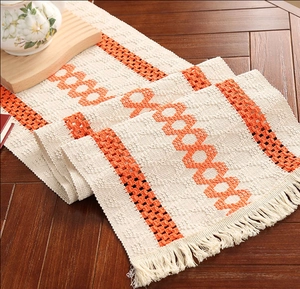 Close-up of beige and orange woven table runner with tassels on a dark wood table