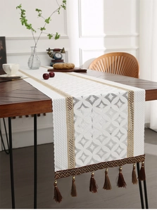 Detail of white lace table runner with geometric weaving and brown fringe tassels