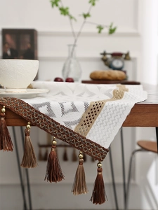 Detail of white lace table runner with brown tassel fringe and golden beads on wood table