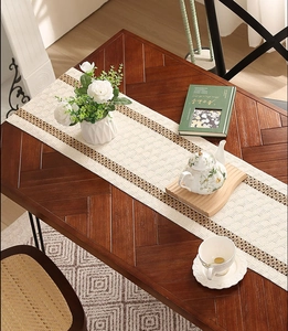 Detailed macro view of cream-white hand-woven table runner with hollow lace tassels