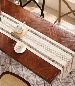 Gros plan d'un chemin de table kaki avec motifs tissés et franges sur table en bois