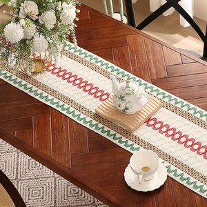 Linen table runner with red and green geometric wave patterns on a dark wood table