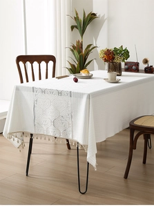 Detail of white hollowed lace tablecloth with vintage scroll patterns and beige tassels