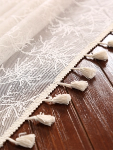 Detailed macro of beige lace tablecloth with branch embroidery and delicate tassels