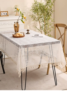 Close-up of white lace tablecloth featuring delicate leaf patterns and beige tassel fringe