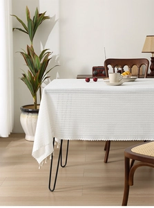 Close-up of white woven tablecloth featuring elegant crochet texture and fringe details