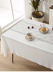 Close-up of thick white lace tablecloth with vintage floral pattern and small tassels