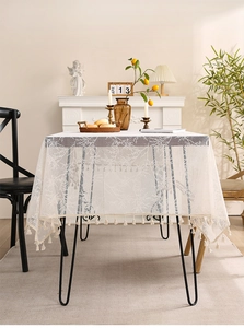 Close-up of cream lace tablecloth featuring botanical branch patterns and fringe tassels