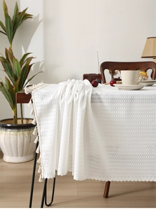 Detailed close-up of white lace tablecloth with decorative tassels on a wooden table edge