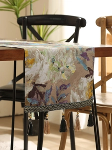 Close-up of abstract floral table runner with vintage tassels on a dark wood table