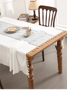 Detailed view of white floral lace tablecloth with elegant tassels on a wooden table