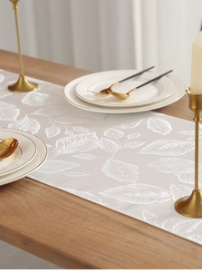 Detailed view of white table runner with elegant leaf patterns on a wooden table
