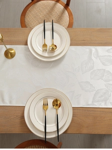 Close-up of beige table runner with leaf jacquard texture and silky sheen on wooden table