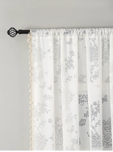 Detail of white French lace curtain featuring floral butterfly patterns and fringe tassels