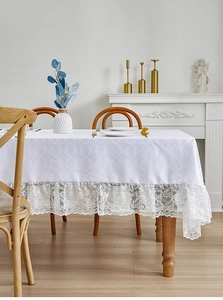 Detailed close-up of white linen tablecloth with leaf jacquard and lace floral borders