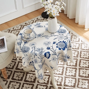 Close-up of round linen tablecloth featuring blue floral patterns and beige tassel fringe