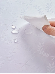 Close-up of waterproof white linen textured tablecloth with embossed leaf patterns