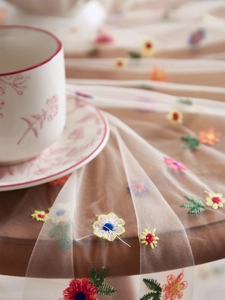 Close-up of colorful floral embroidery on transparent white lace mesh tablecloth fabric