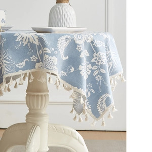 Detail der blau-leinenen Tischdecke mit weißem Blumenmuster und eleganten Fransen