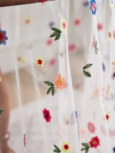 Macro shot of colorful floral embroidery on white transparent lace tablecloth fabric