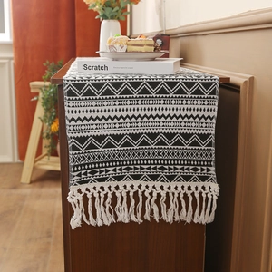 Bohemian black and white geometric woven table runner with white tassels on a wooden table