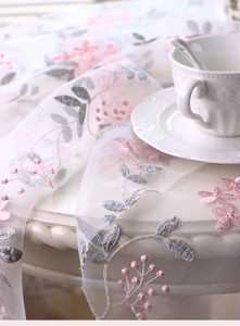 Close-up of elegant floral embroidery on white lace tablecloth with pink flower detail
