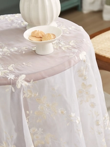 Detailed close-up of white lace floral embroidery on translucent mesh tablecloth