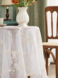 Detailed close-up of white lace tablecloth with yellow floral embroidery on a wood table