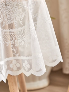 Macro shot of white lace tablecloth featuring delicate floral hollow embroidery and scalloped edges
