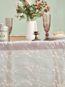 Detail einer eleganten Spitzen-Tischdecke mit rosa Pflaumenblüten-Stickerei und Netzstruktur
